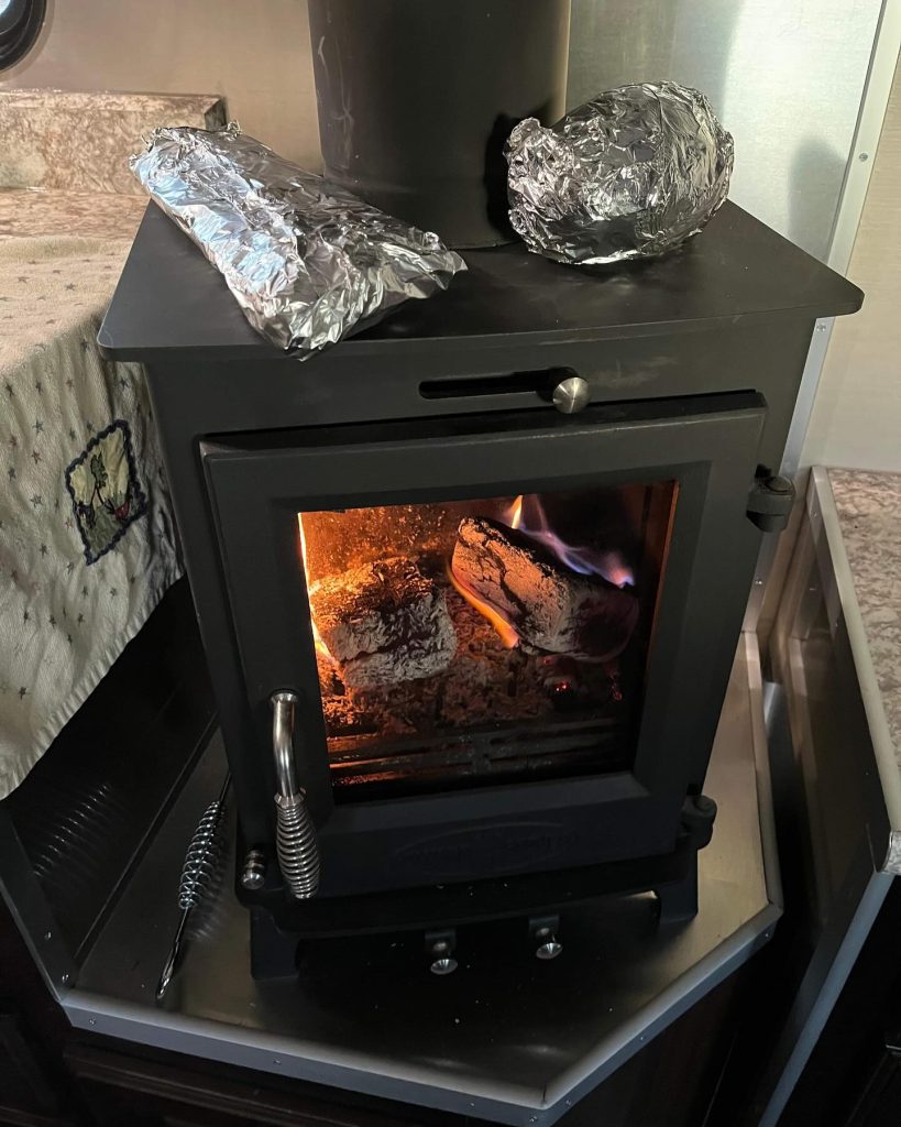 Wood-burning stove with a fire and foil-wrapped food inside a real camp trailer