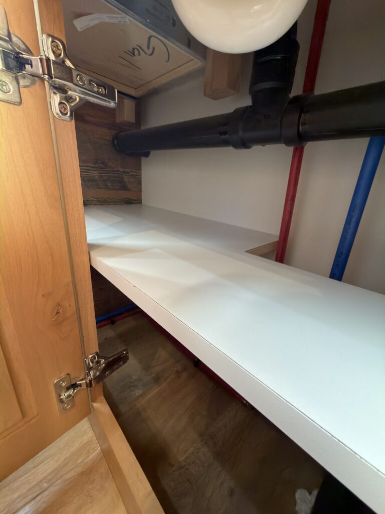 Image of the bathroom cabinet shelves and plumbing of Gail Camp #131.