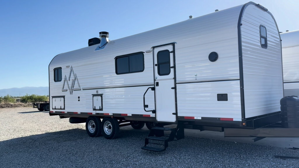 Plankis Camp #124 viewed from the entry side, with windows, roof vents, steps, and tandem wheels visible.