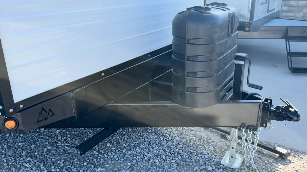 Black trailer tongue on Plankis Camp #124 with a propane cover, coupler, safety chains, and tongue jack.