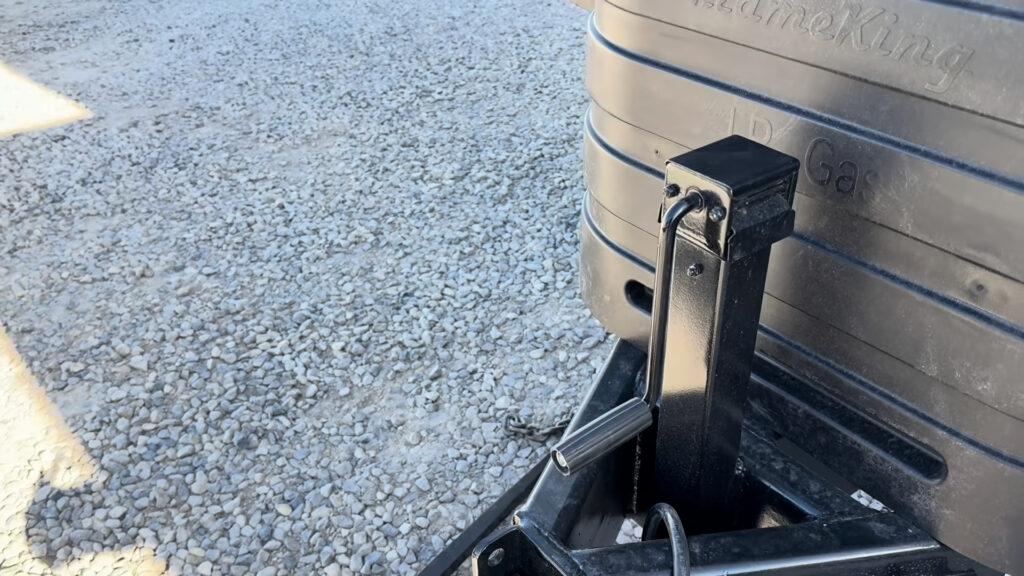 Black tongue jack with a crank handle in front of the propane cover on Plankis Camp #124.