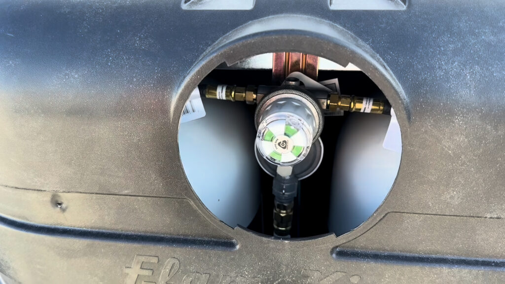 Propane regulator and hoses visible through the round opening in the cylinder cover on Plankis Camp #124.