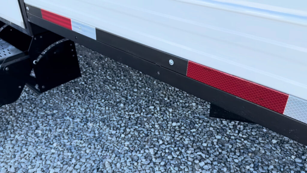 Skirting rail and red and white reflectors along the black lower trim of Plankis Camp #124, beside the entry steps.