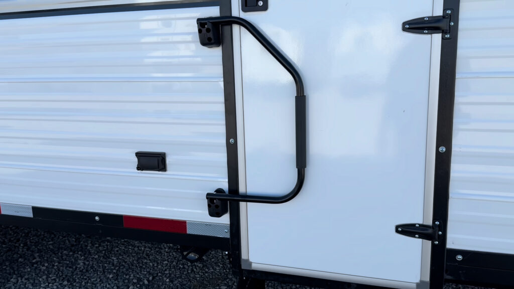 Black grab handle mounted beside the white entry door and black door frame on Plankis Camp #124.