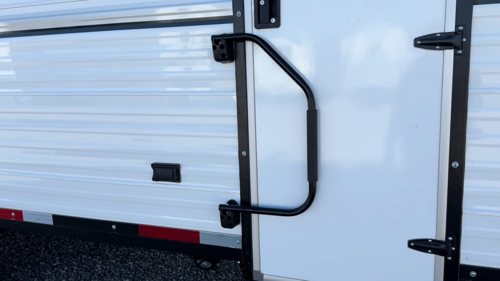 Entry grab handle and black hinges on the white side door of Plankis Camp #124.