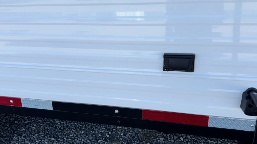 Covered black AC outlet near the entry door, above the reflective lower trim on Plankis Camp #124.