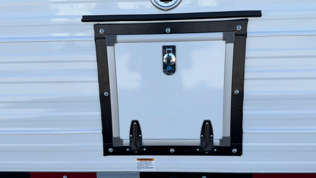 Closed white wood box hatch with a latch, black frame, and lower hinges on Plankis Camp #124.