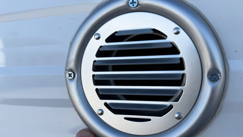 Round silver louvered air intake vent for the wood-burning stove on the exterior of Plankis Camp #124.