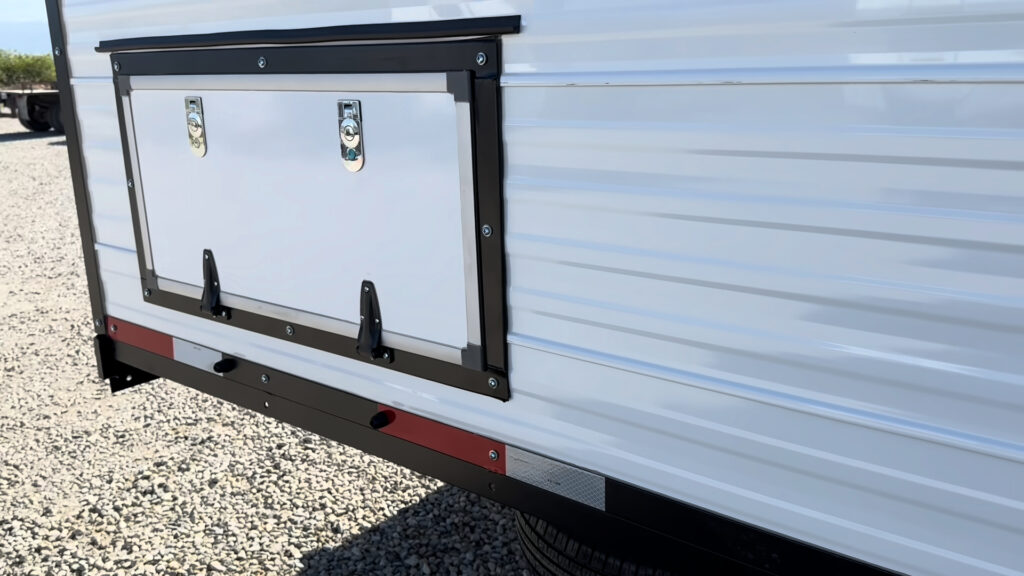 Wide white storage hatch with two latches and black trim along the side of Plankis Camp #124.
