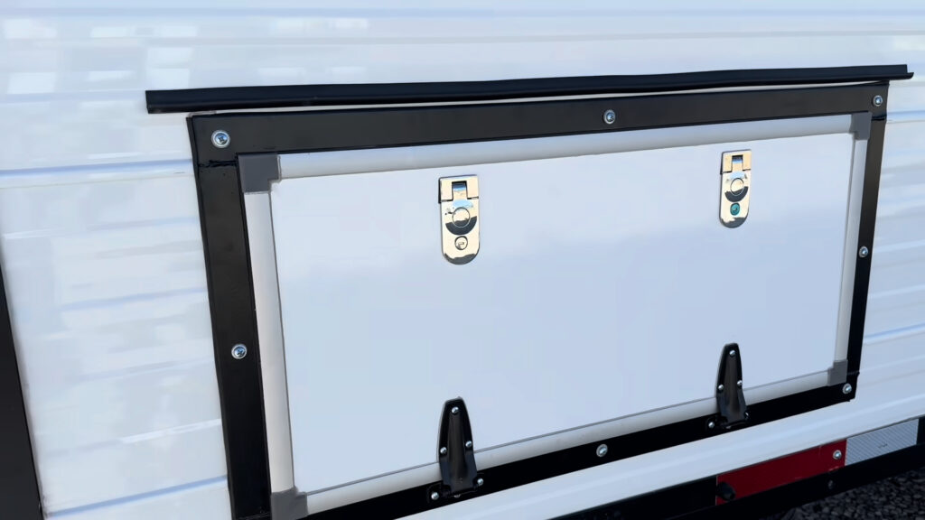 Two latches and three lower hinges on a wide white exterior storage hatch on Plankis Camp #124.