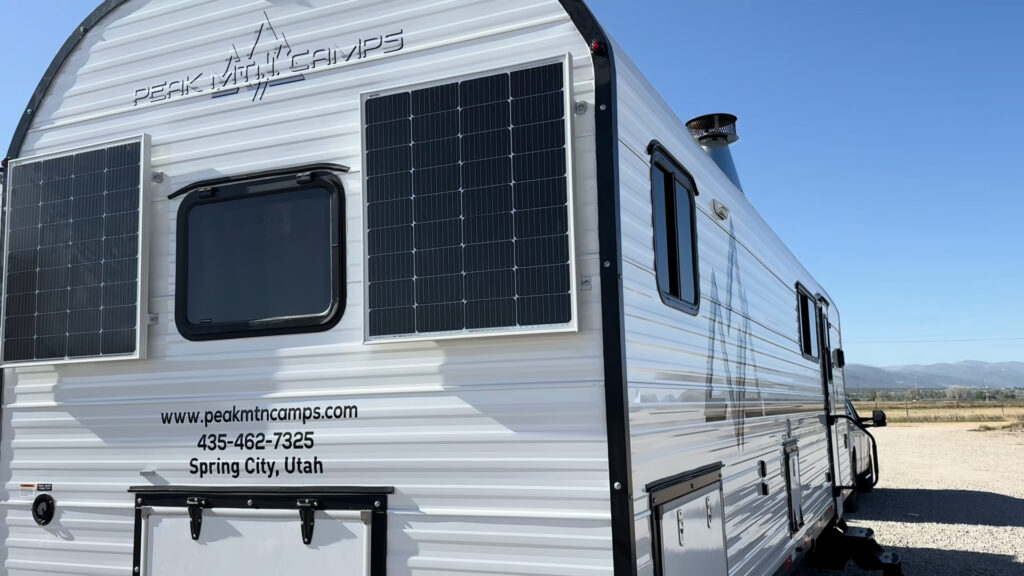 Two solar panels flank the rear window beneath the Peak Mountain Camps logo on Plankis Camp #124.
