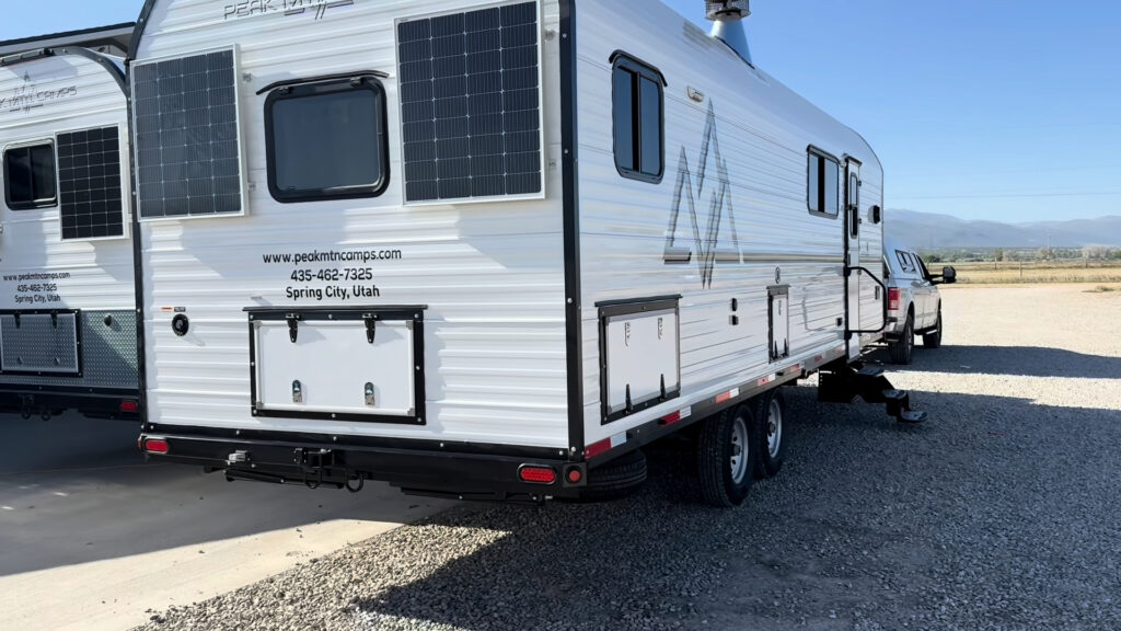 Rear three-quarter view of Plankis Camp #124 with two solar panels, storage hatches, tandem wheels, and a bumper.