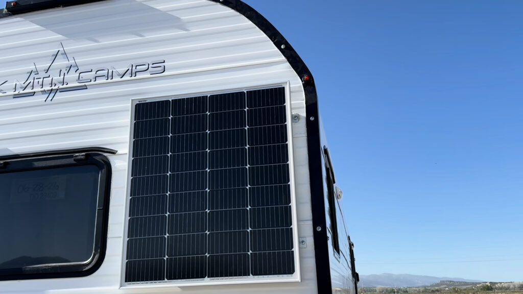 Close view of a solar panel beside the rear window and curved black roof trim on Plankis Camp #124.