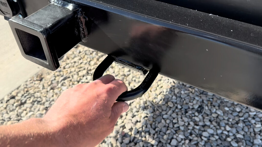 A hand holds a metal loop beside the square receiver on the rear bumper of Plankis Camp #124.