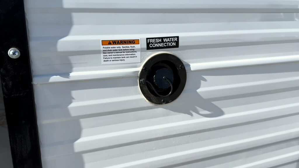 Round capped inlet labeled Fresh Water Connection on the white exterior wall of Plankis Camp #124.