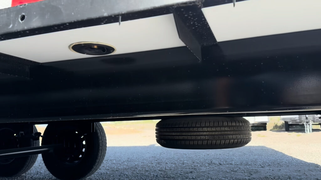 Spare tire mounted horizontally beneath Plankis Camp #124, with the city water connection visible under the body.