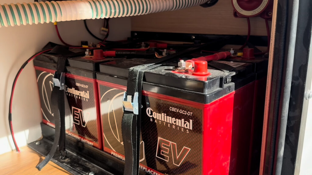Red and black batteries with connected cables and retaining straps inside a compartment on Plankis Camp #124.