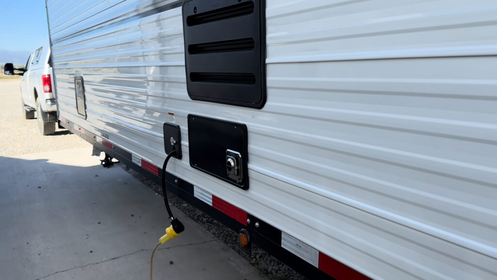 Road-side vents, service panels, and a connected power cord along the white siding of Plankis Camp #124.