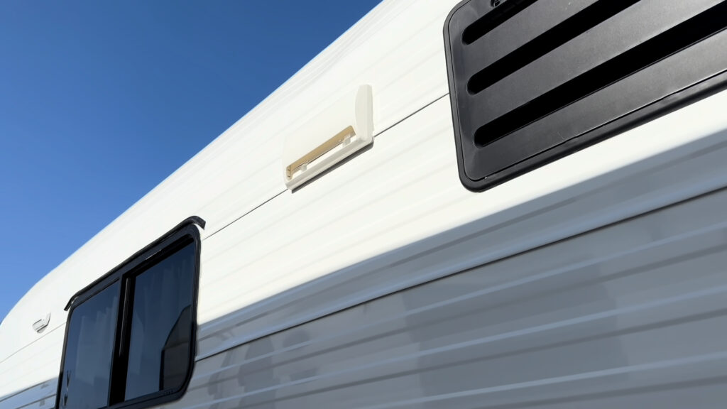 Exterior light and range hood vent mounted high on the side wall beside a window on Plankis Camp #124.
