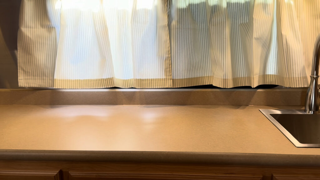 Kitchen countertop below striped curtains in Plankis Camp #124, with the sink edge visible at the right.