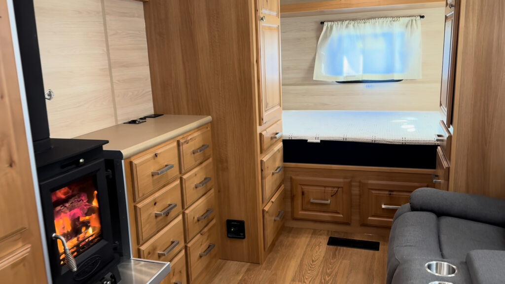 Interior of Plankis Camp #124 with a black stove, wood drawers, seating, and a bed between tall cabinets.
