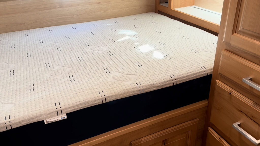 Close view of the mattress and raised wood bed base beside drawers and open shelving in Plankis Camp #124.