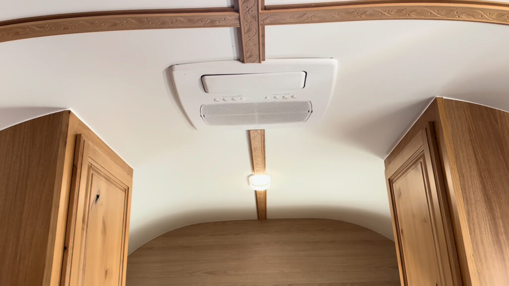 White ceiling air conditioner between carved wood trim strips above the sleeping area in Plankis Camp #124.