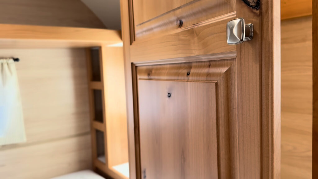 Raised-panel wood wardrobe door with metal hardware beside the sleeping area in Plankis Camp #124.