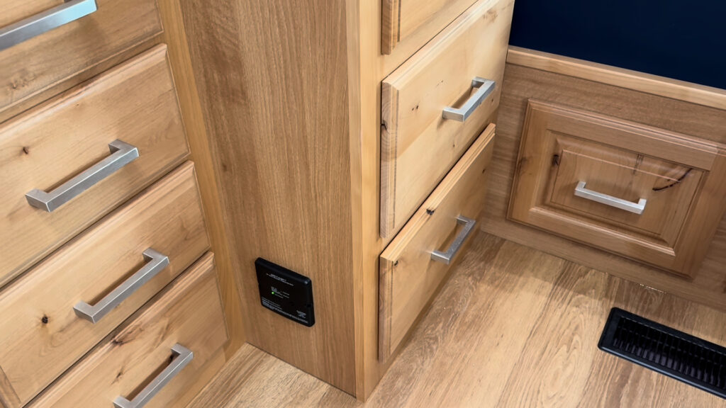 Wood drawer banks with metal pulls beside the bed and aisle floor vent in Plankis Camp #124.
