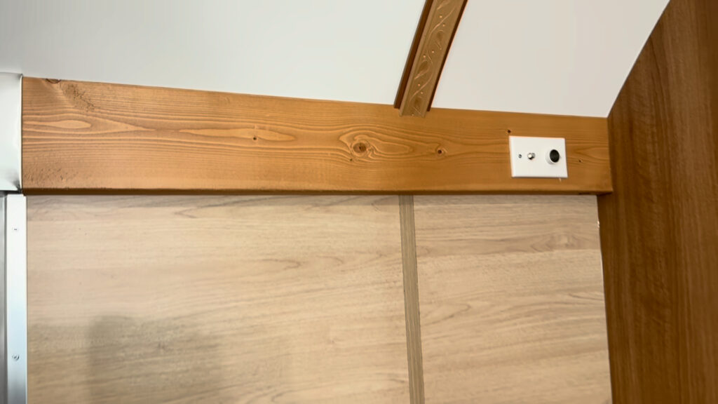 Small white connection plate mounted on the wood trim below the curved ceiling in Plankis Camp #124.