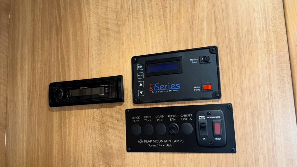 Stereo, monitoring displays, tank indicators, and labeled switches mounted on a wood wall in Plankis Camp #124.