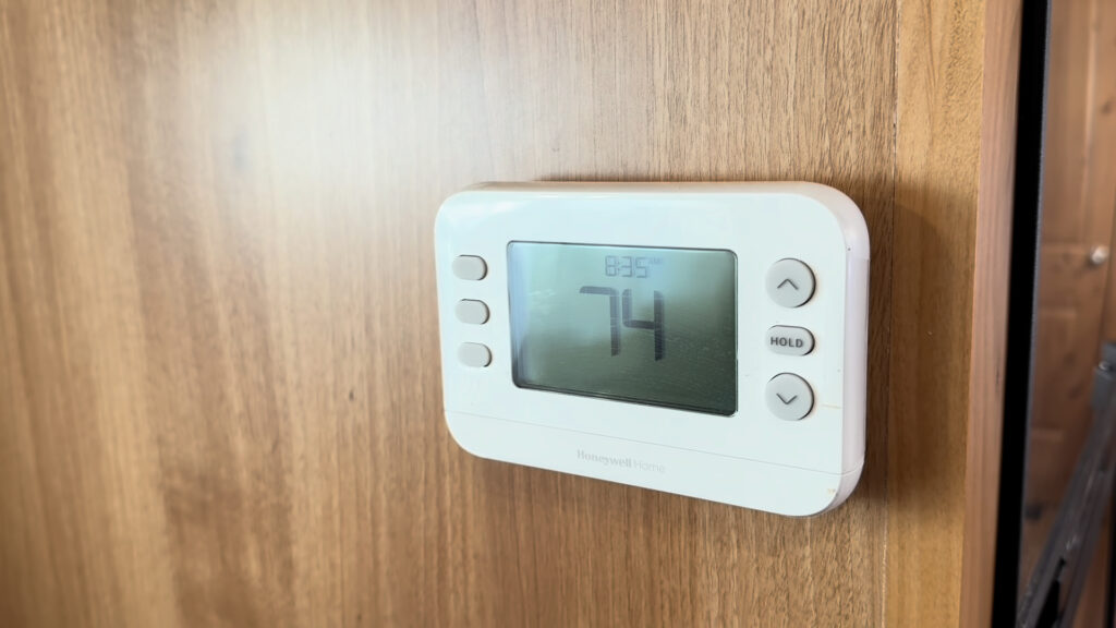 White digital thermostat displaying 74 on the wood wall inside Plankis Camp #124.