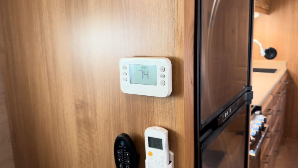 White thermostat and mounted remotes on a wood partition beside the refrigerator in Plankis Camp #124.