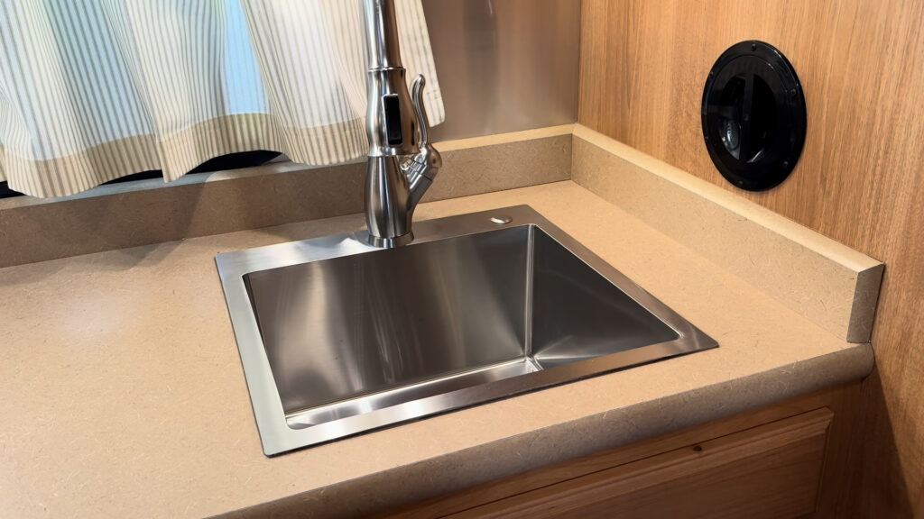 Rectangular stainless steel kitchen sink with a tall faucet below striped curtains in Plankis Camp #124.