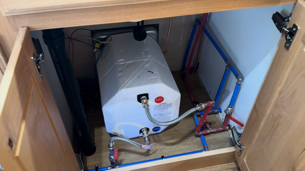 Water heater and plumbing inside the open wood sink cabinet of Plankis Camp #124.