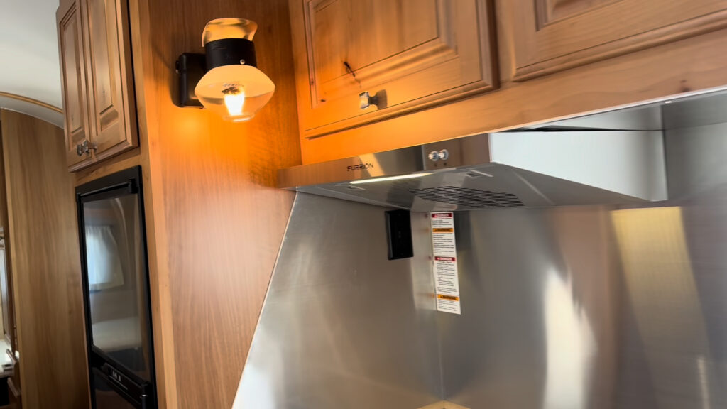 Lit propane wall light beside wood cabinets and a stainless range hood in Plankis Camp #124.