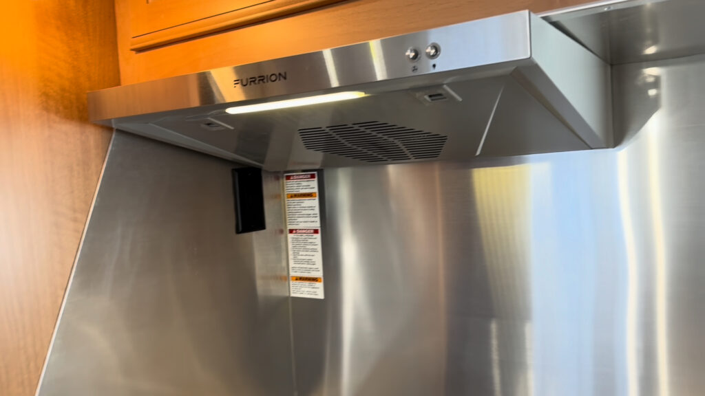 Stainless Furrion range hood with a visible fan grille above a metal backsplash in Plankis Camp #124.