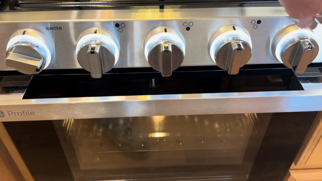 Metal range control knobs above a glass-front oven door in the kitchen of Plankis Camp #124.
