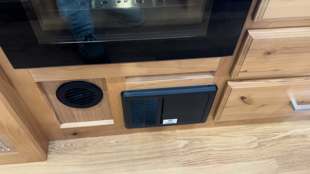 Round black vent and rectangular electrical panel beneath the oven in Plankis Camp #124.