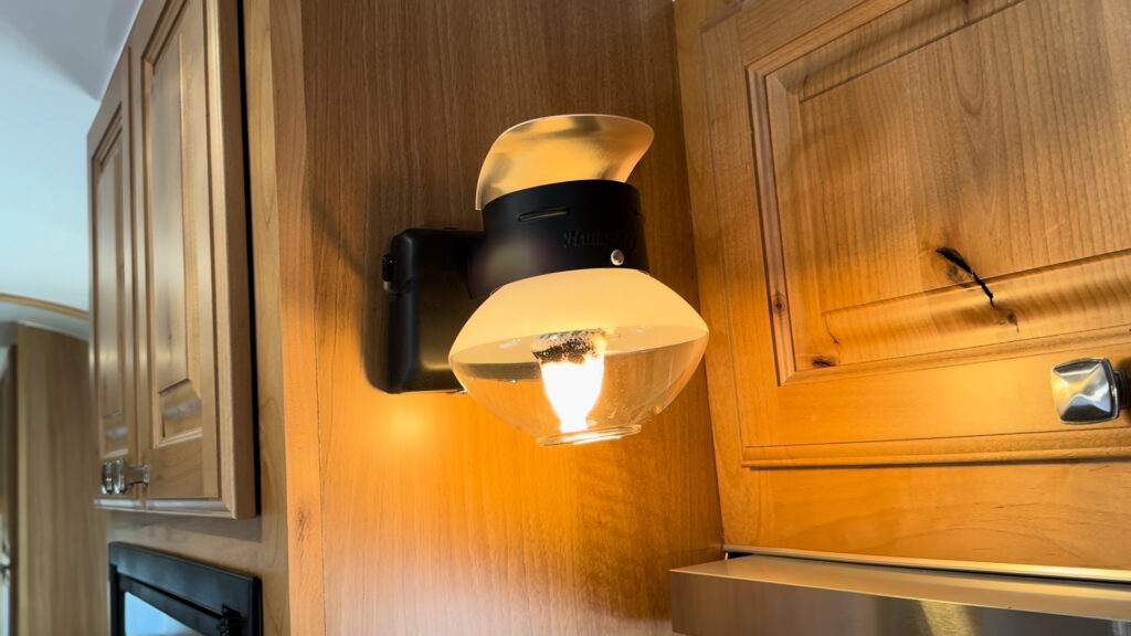 Lit black and brass-colored propane gas light between wood cabinets inside Plankis Camp #124.