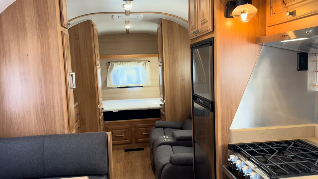 Lit propane gas light and range frame a view past the dinette toward the bed in Plankis Camp #124.