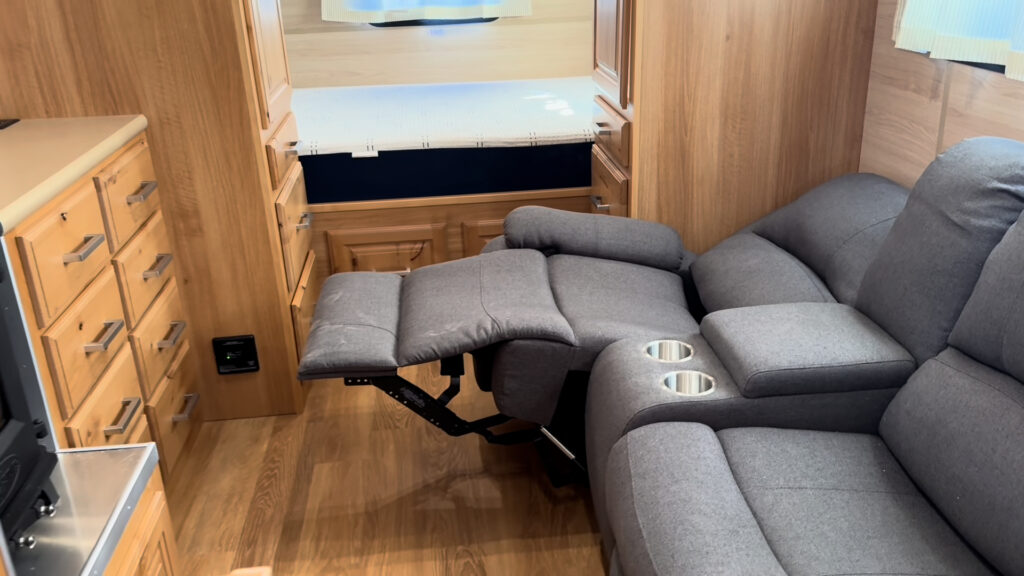 Reclining loveseat with one footrest extended beside the wood drawers and bed in Plankis Camp #124.