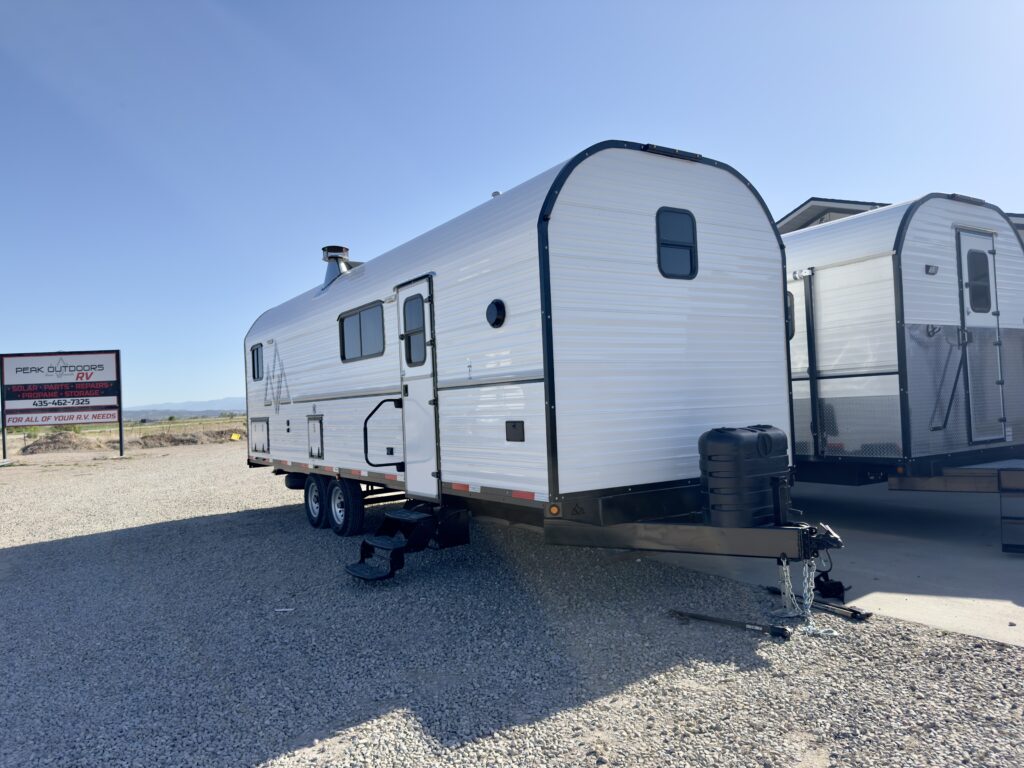 Front three-quarter view of Plankis Camp #124 with a curved front wall, entry steps, propane cover, and hitch.