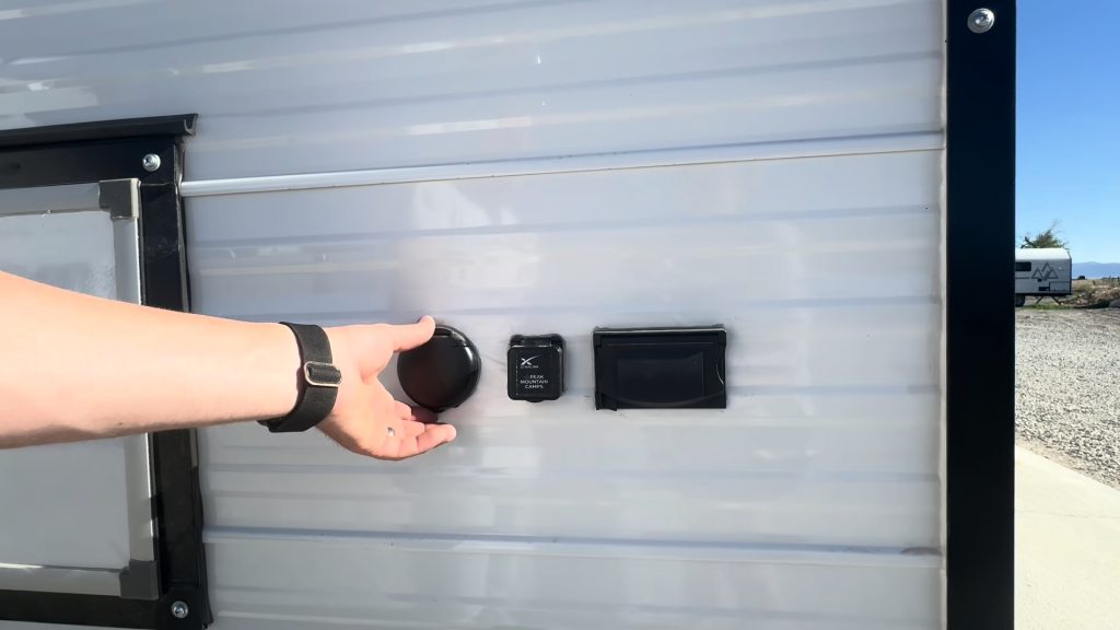 Close view of exterior hookup ports beside a storage hatch.