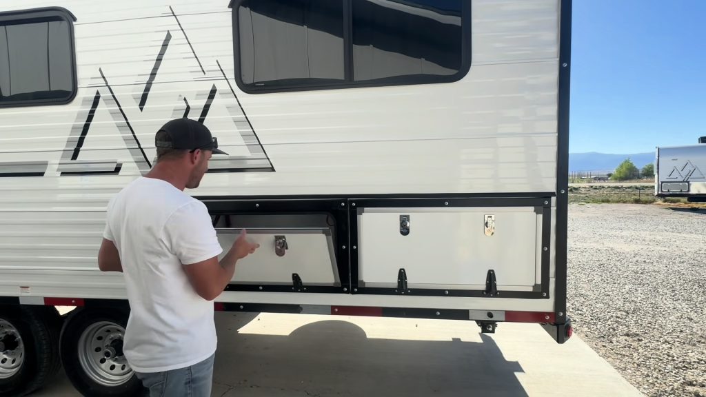 Presenter beside two open exterior storage compartments above the dual axles.