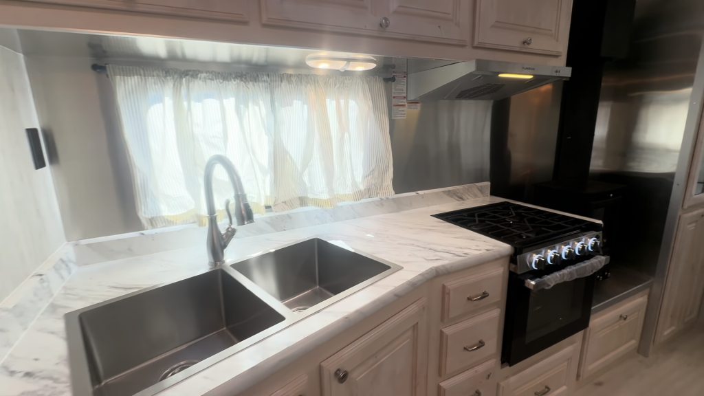 Kitchen counter with stainless steel double sink, window, range, and cabinets.