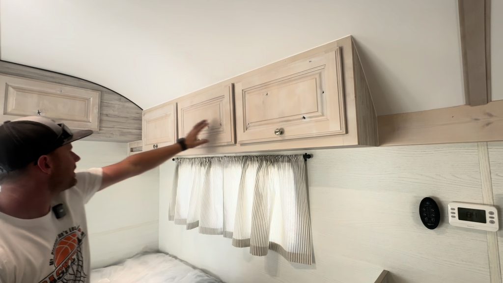 Presenter pointing to overhead cabinets above the rear sleeping area.