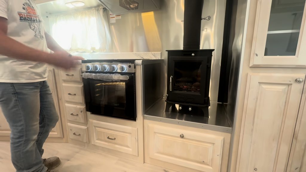 GE range beside the black wood-burning stove and light-colored kitchen cabinets.