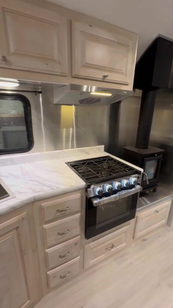 Portrait view of the three-burner range, wood stove, and pale cabinetry.