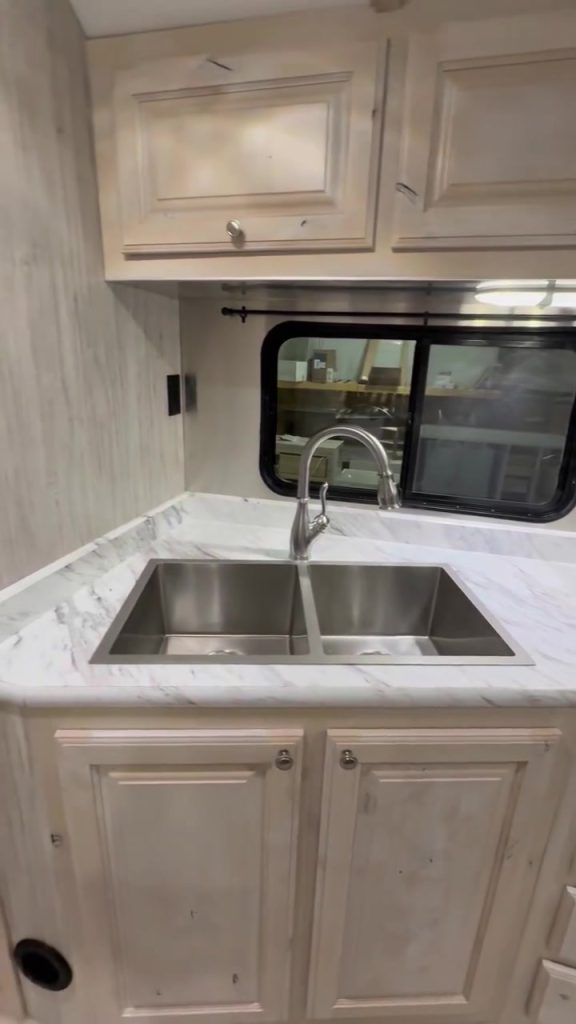 Portrait view of the double sink, faucet, countertop, and kitchen window.